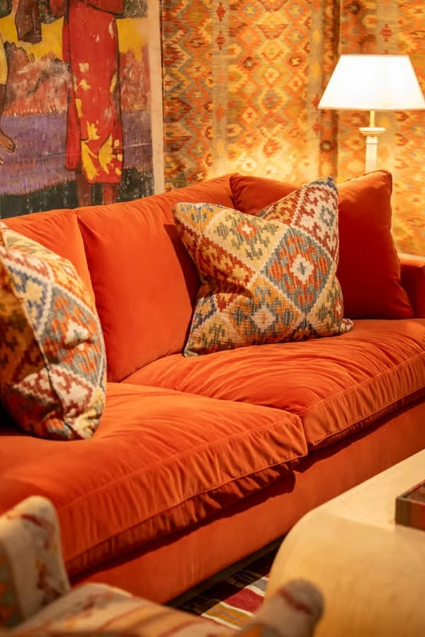 British luxury interior design featuring burnt orange velvet sofa, embroidered geometric cushions, and richly patterned designer wallpaper and fabrics.